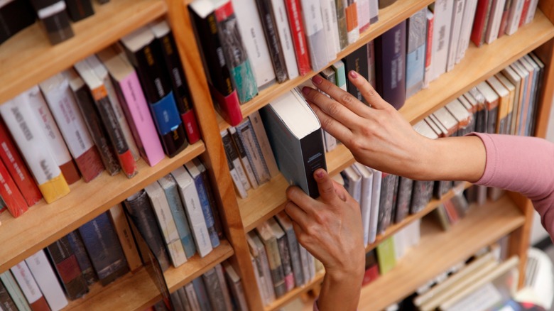 Hands pulling a book from a bookshelf