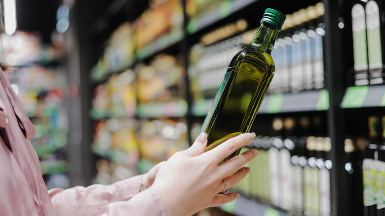 Feminine hands holding an olive oil bottle in store aisle