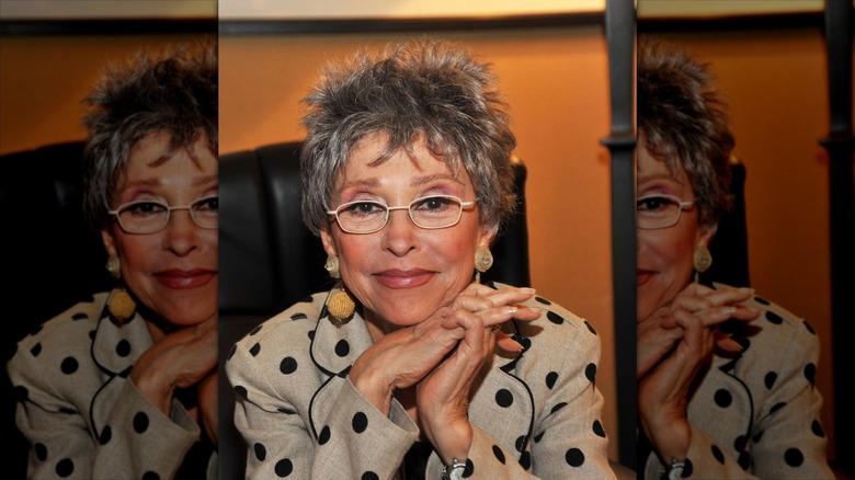 Rita Moreno smiles wearing a polka dot blazer and a gray pixie cut