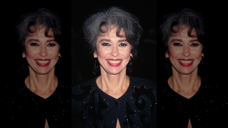 Rita Moreno smiles with gray-black hair and red lipstick
