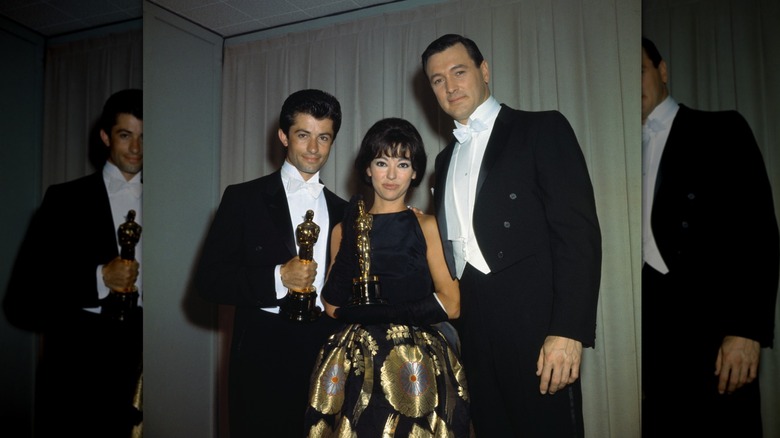 Rita Moreno holding an Oscar while posing with two men