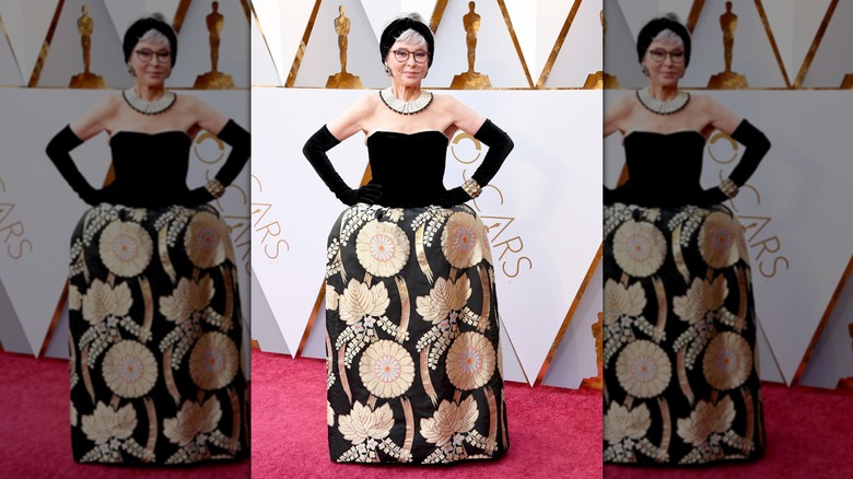 Rita Moreno on the red carpet in a black strapless gown with gold flowers printed on the skirt