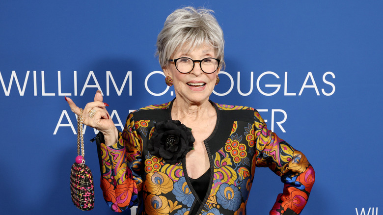 Rita Moreno on the red carpet holding up a purse with one finger