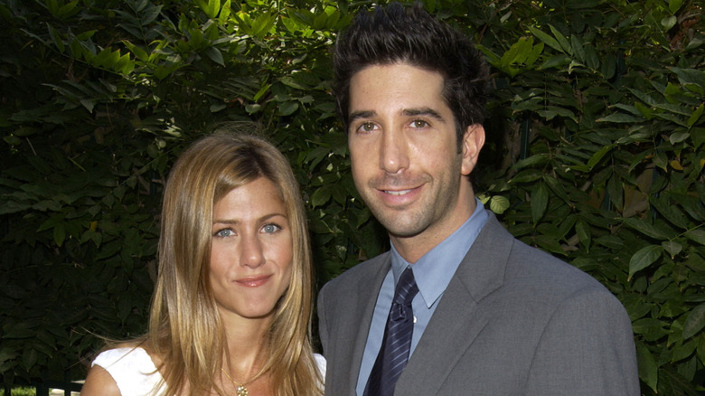 Jennifer Aniston standing with David Schwimmer in front of leaves