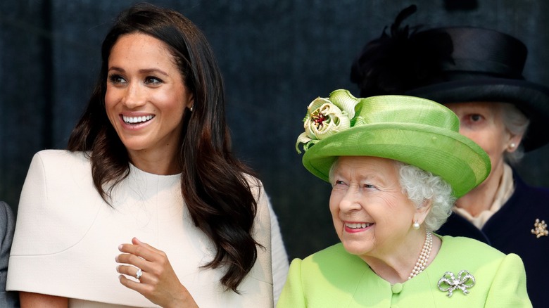 A hatless Meghan Markle next to Queen Elizabeth II in a green hat