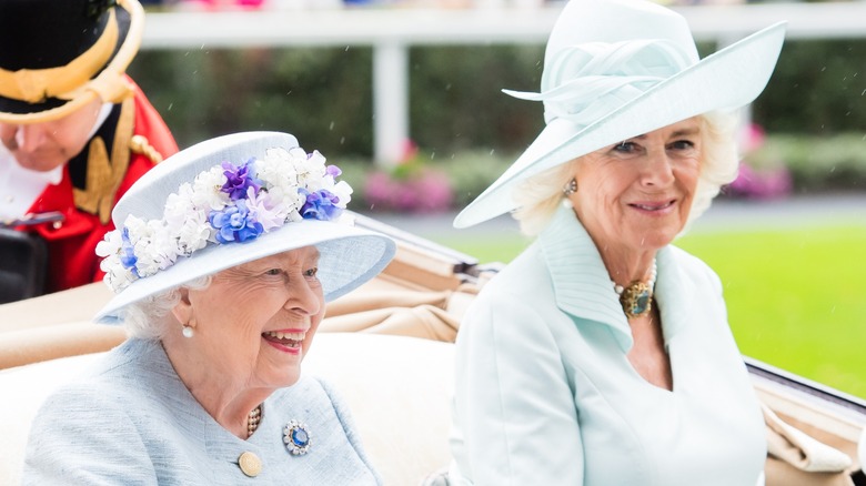 Queen Elizabeth II and Queen Camilla both wearing light blue while riding in a carriage together