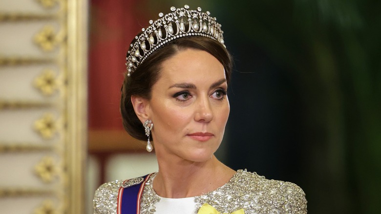 Kate Middleton wearing an embellished dress and a large tiara with a neutral expression