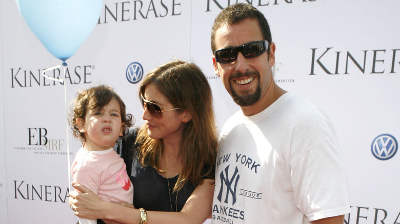 A young Sadie Sandler holds a blue balloon next to Adam Sandler in sunglasses