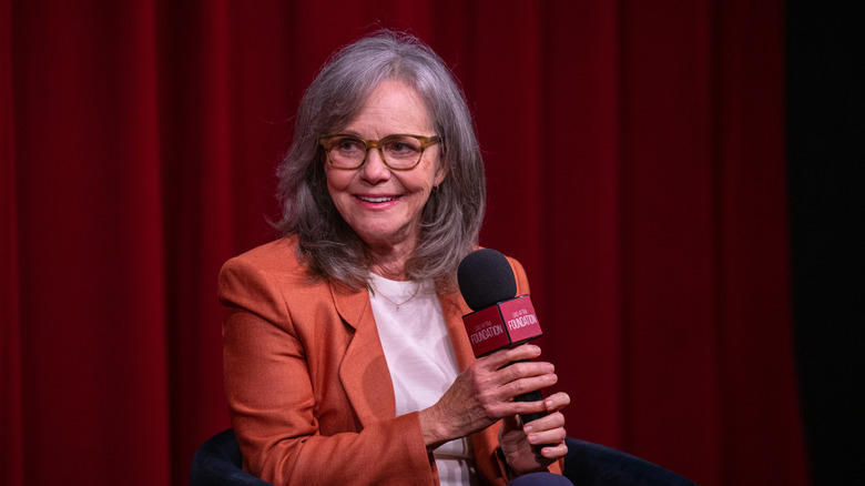 Sally Field in an orange blazer and holding a mic