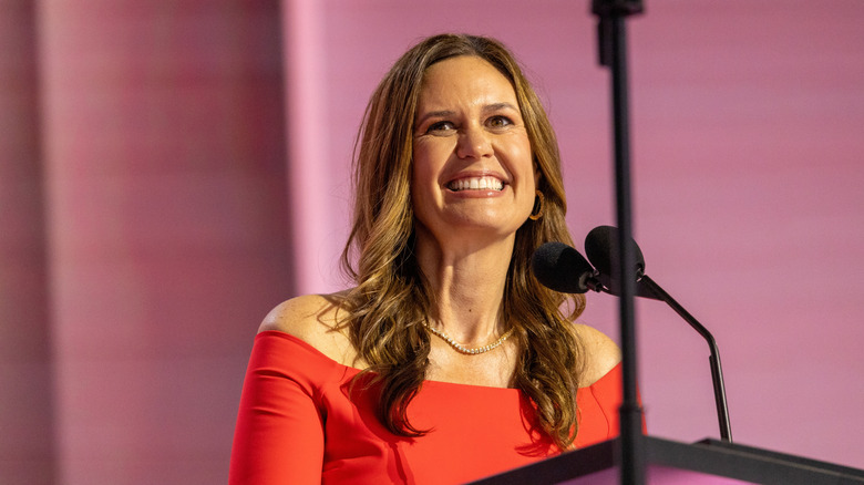 Sarah Huckabee Sanders speaking at a podium in a red dress