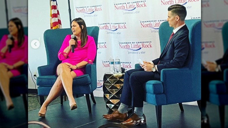 Sarah Huckabee Sanders sitting onstage with another man nearby