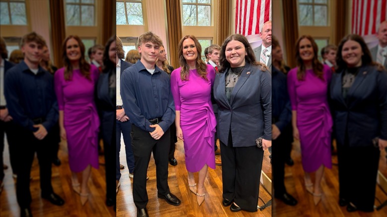 Sarah Huckabee Sanders in a magenta dress and nude heels posing with two people