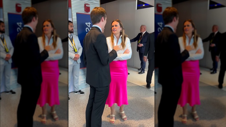 Sarah Huckabee Sanders wearing a pink skirt and off-white sandals while talking to a young man in a suit