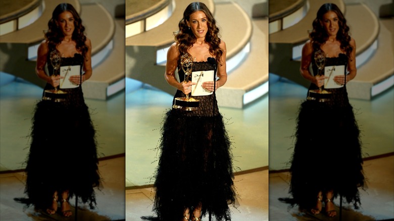 Sarah Jessica Parker speaks into a microphone wearing a black feather skirt