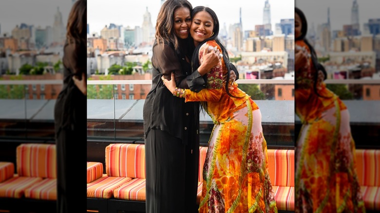 Michelle Obama wears an all-black outfit while hugging Sasha Obama in an orange maxi dress