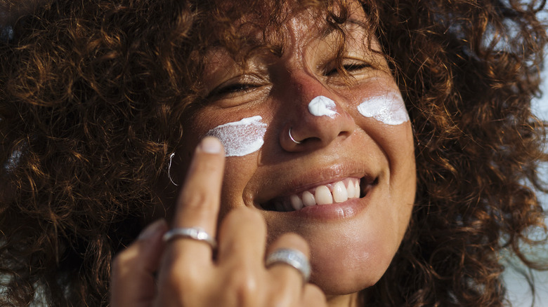 Woman with curly hair smiling and applying sunscreen
