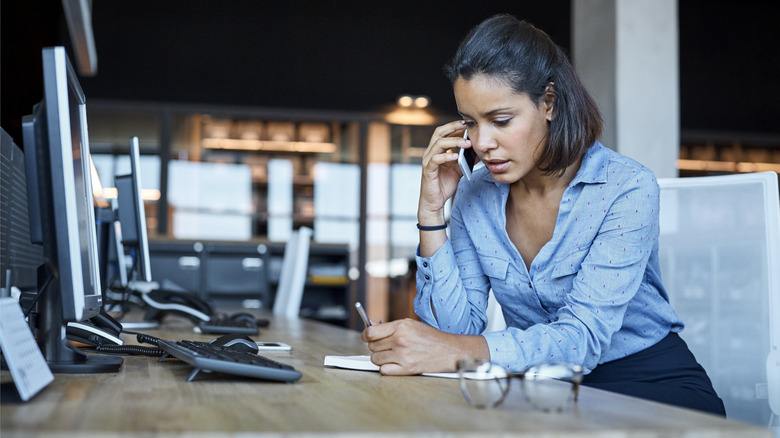 Woman on a phone call and writing in a notebook