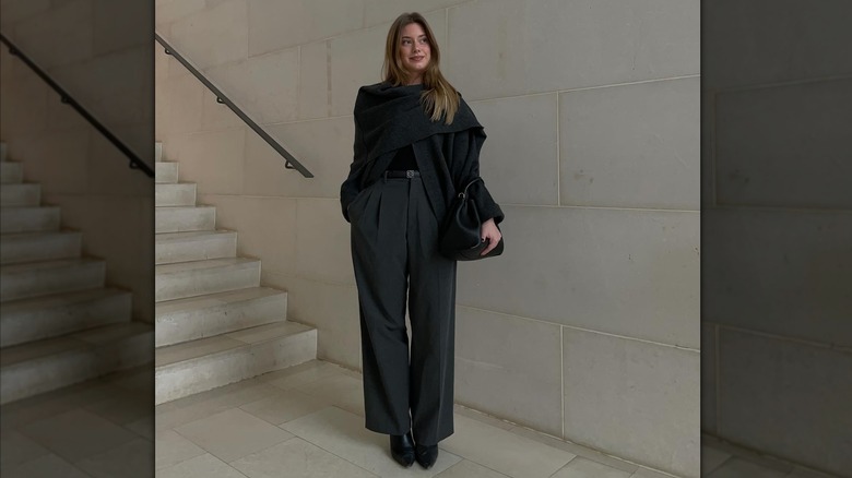 A woman wearing a black scarf cardigan with black pants