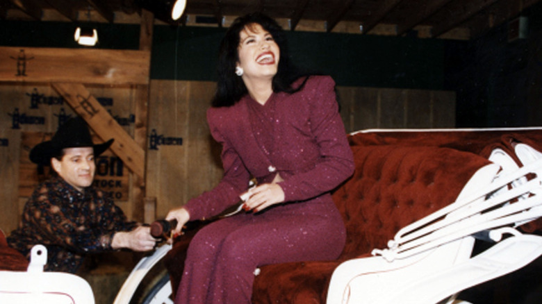 Selena riding in a carriage at the Houston Livestock Show & Rodeo while wearing a sparkly, red bodysuit