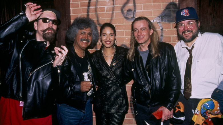 Selena posing with a group of men at the Hard Rock Cafe while wearing a sparkly, striped suit