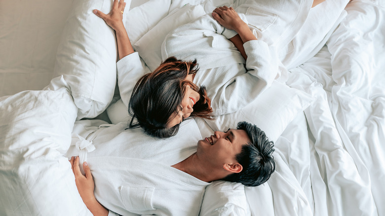 A couple smiles at each other while laying in bed