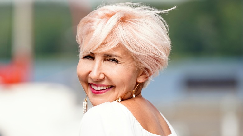 An older woman with a light pink bixie cut smiles at the camera