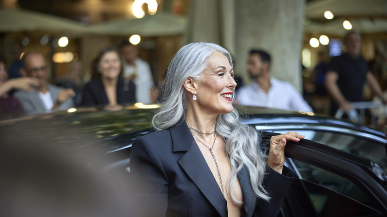 A gray-haired woman steps out of her car and poses for photos