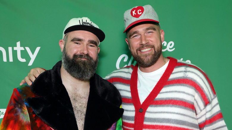 Travis and Jason Kelce wearing brightly colored outfits in front of a step-and-repeat