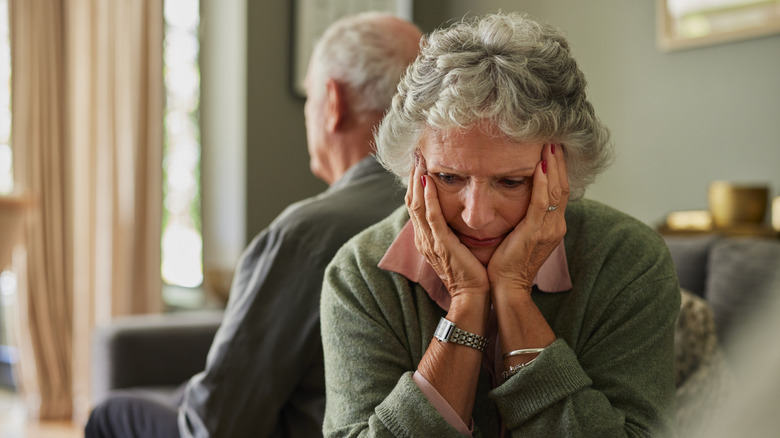 A senior couple have their backs against each other and the woman shows frustration