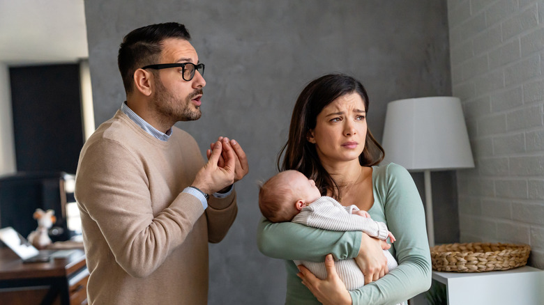 Young unhappy father with baby and wife suffering from postnatal depression at home