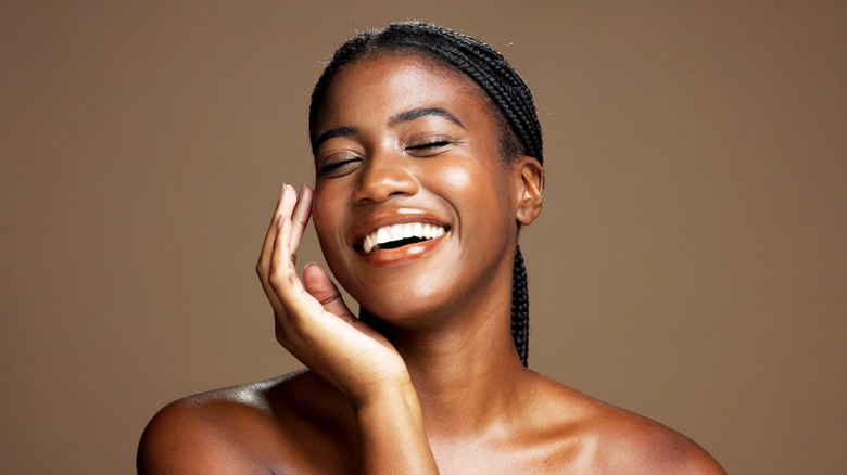 A woman with glowing skin is touching her face and smiling