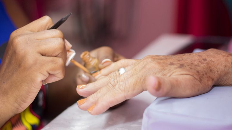 A close-up of a manicurist painting an older woman's nails.