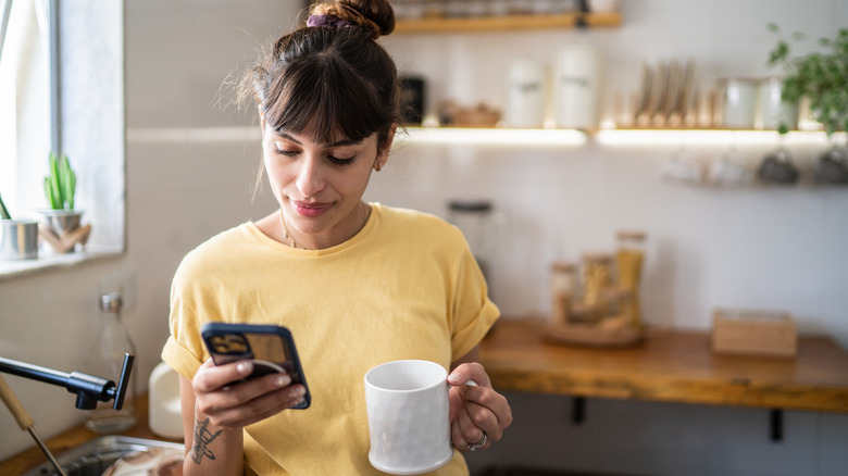 Woman holding mug looking at phone