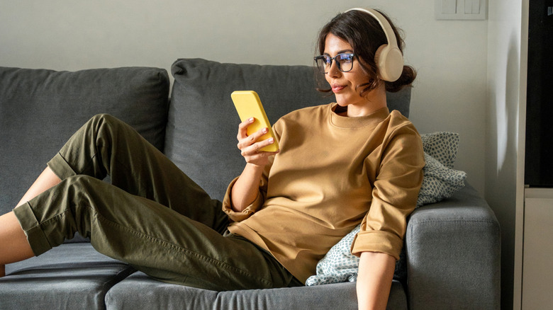 Woman lying on couch using her phone and listening to audiobook