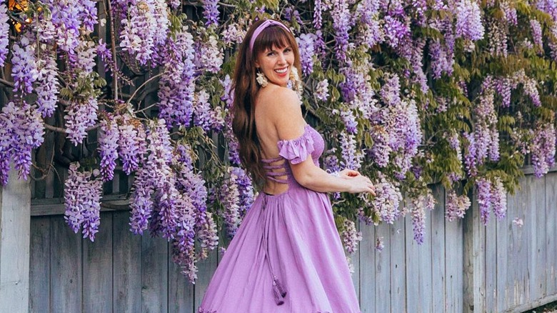 A woman in a lilac dress next to a wisteria plant