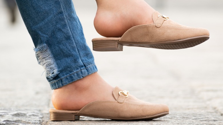 A person wearing nude, backless loafers with blue jeans