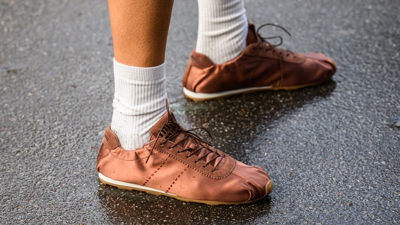 A person wearing slimline, brown, satin sneakers