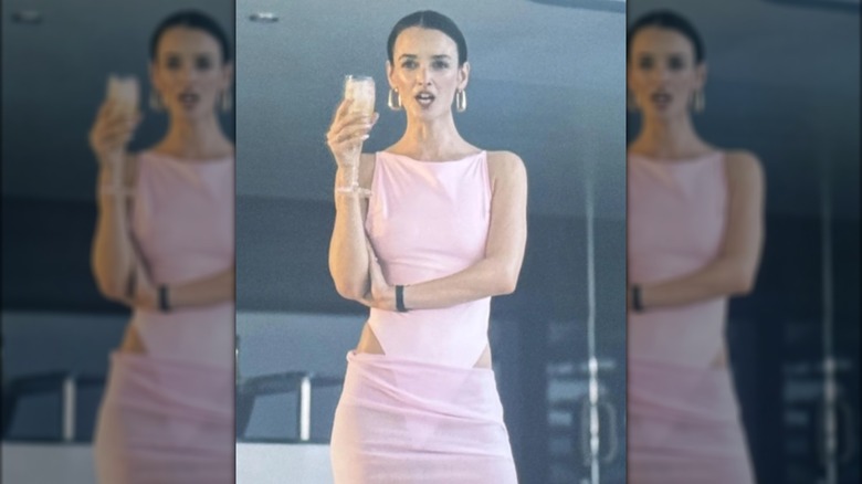 Woman wearing a pink bathing suit and pink skirt holding a glass of champagne