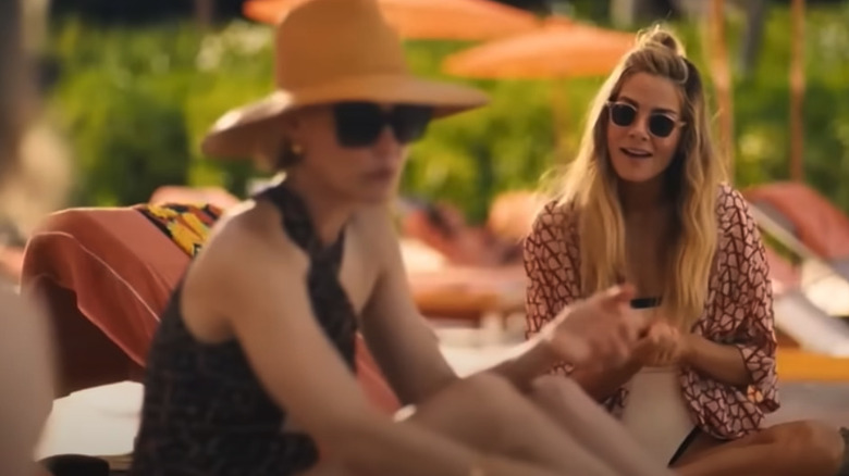 Two women wearing bathing suits and coverups on poolside lounge chairs