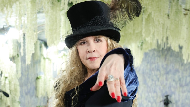Stevie Nicks posing with her hand toward the camera while wearing a black top hat