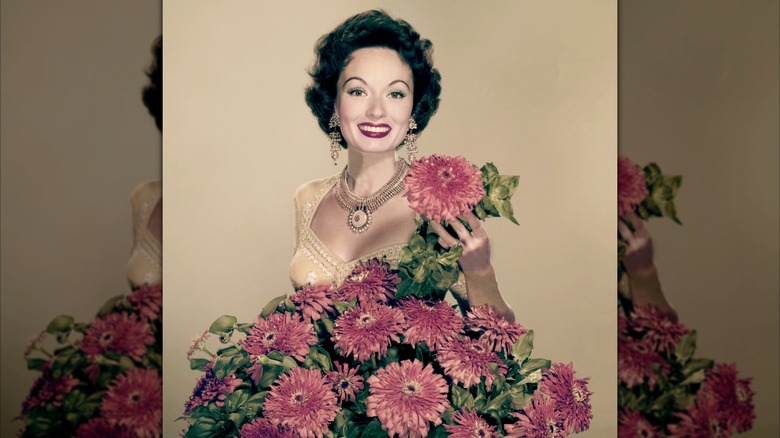 Ann Blyth smiling standing in front of a large flower arrangement in 1956