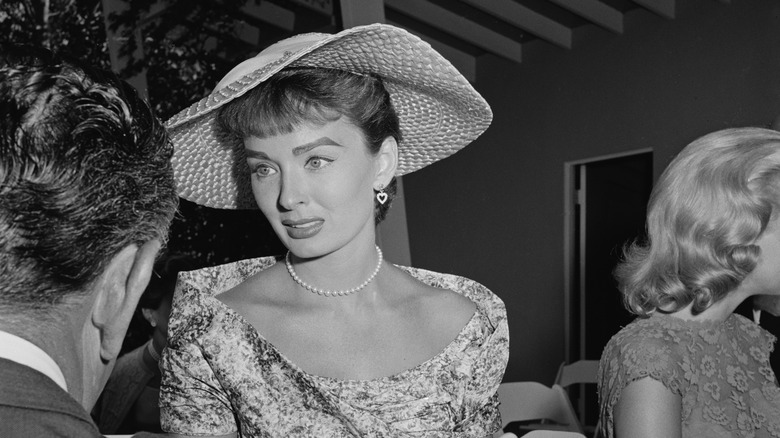 A black and white photo of Ann Blyth speaking to a man at a party