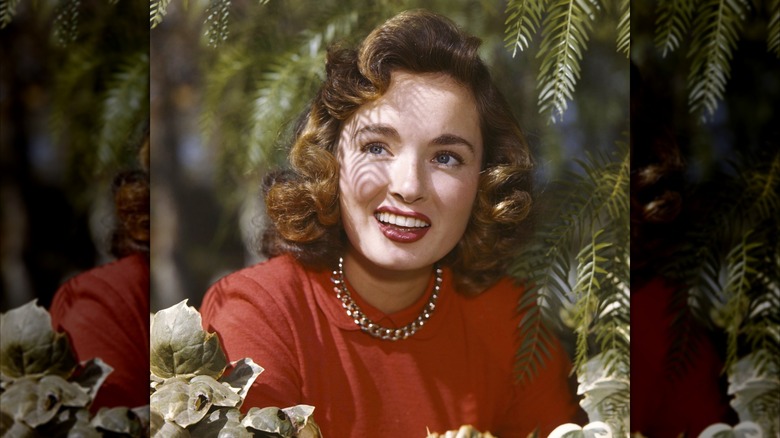 Ann Blyth in a red sweater surrounded by green branches