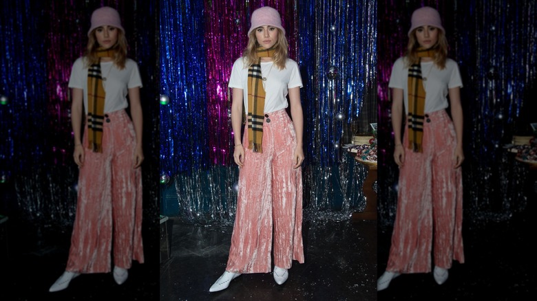 Suki Waterhouse waring a white t-shirt, velvet jeans, a scarf, and a bucket hat at a Christmas event