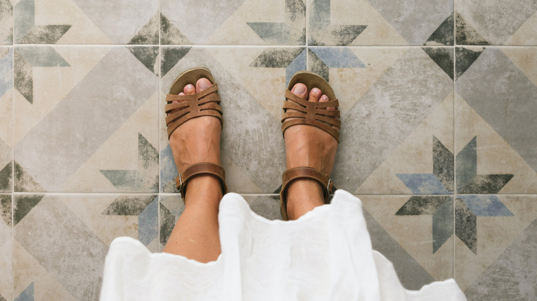 A top view of a women's feet in sandals on a tile floor