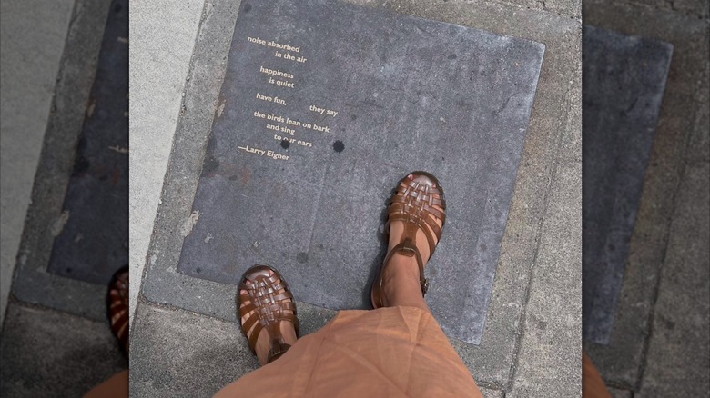 A shot looking down at a women's jelly sandal shoes on the sidewalk next to an inscribed quote