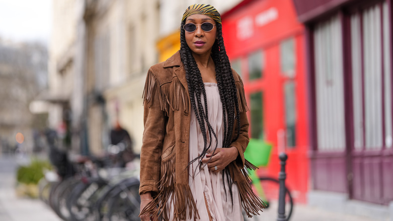 A woman in a brown fringe jacket and a pale pink dress with a headband