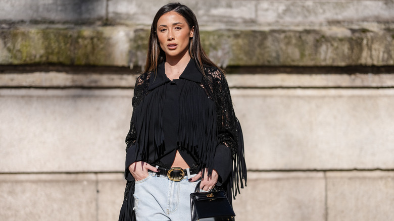 A woman in light wash jeans with a black tassel top outside