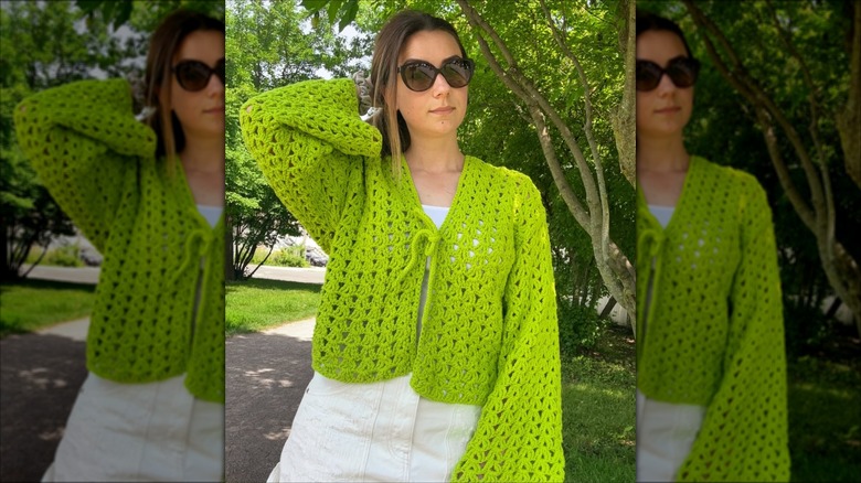 A woman wearing a lime green tie-up cardigan with white jeans and sunglasses