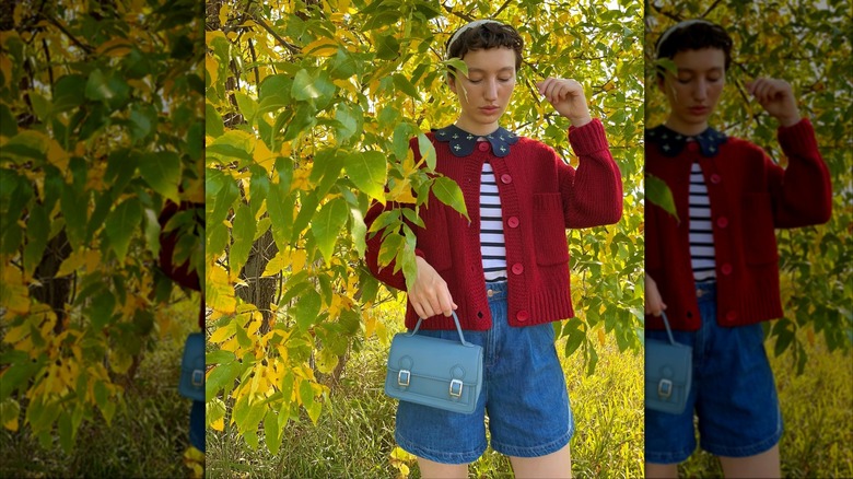 A woman in a forest wearing a red cardigan, jean shorts and a Peter Pan blouse